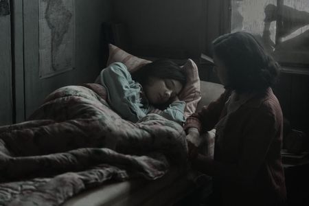 A SMALL LIGHT - Anne, played by Billie Boullet, sleeps as Miep, played by Bel Powley, watches over her in A SMALL LIGHT. (Credit: National Geographic for Disney/Dusan Martincek)