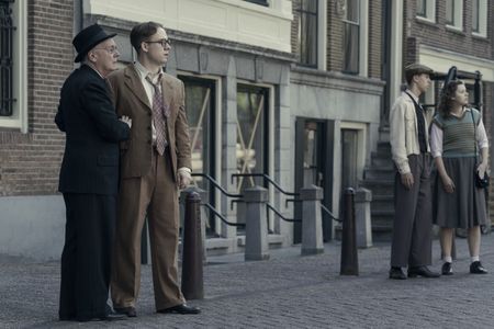 A SMALL LIGHT - Nels, played by Jeffrey Rawle, and Jan, played by Joe Cole, gaze across the canal to the Opekta office as seen in A SMALL LIGHT. (Credit: National Geographic for Disney/Dusan Martincek)