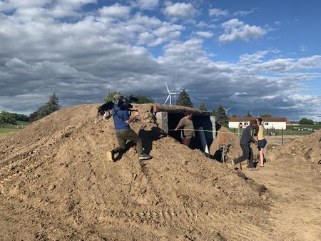 Charles Pol, Ben Reinhold, and Beth Pol measure the farm's new sheep hut with a tape measure while Dax, Ben's dog, watches and a crew member films them. (National Geographic )