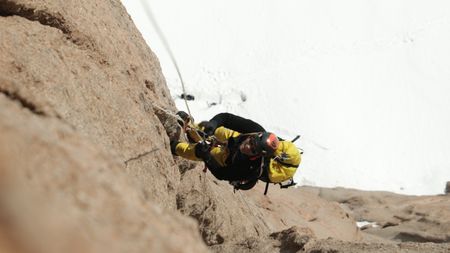 Professional alpinist Conrad Anker climbs a mountain in Queen Maud Land, in Antarctica. Anker holds onto a rope hundreds of feet above the snow-covered ground.  (credit: National Geographic/Cedar Wright)