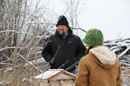 Charles Pol smiles with Beth Pol by the Pol family's beehives, after setting up large hay bales as a barrier to protect the hives from strong winter winds. (National Geographic)