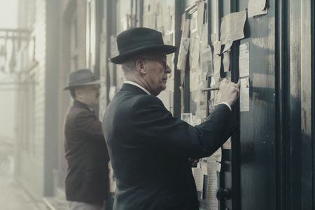 A SMALL LIGHT - Mr. Kugler, played by Nicholas Burns, and Mr. Kleiman, played by Ian McElhinney, plaster posters looking for Anne and Margot Frank as seen in A SMALL LIGHT. (Credit: National Geographic for Disney/Dusan Martincek)