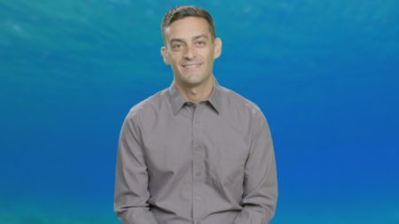 Marine Biologist Andrew Nosal lends a hand explaining shark behavior against the background of a water column. (National Geographic)