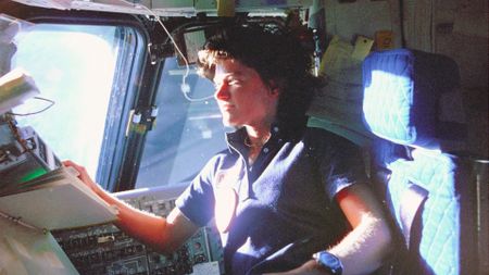 Astronaut Sally Ride, mission specialist on STS-7, monitors control panels from the pilot's chair on the Flight Deck. Floating in front of her is a flight procedures notebook. (Credit: NASA)